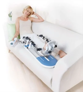 Kobieta korzystająca z szyny CPM do rehabilitacji kolana, siedząc wygodnie na kanapie.