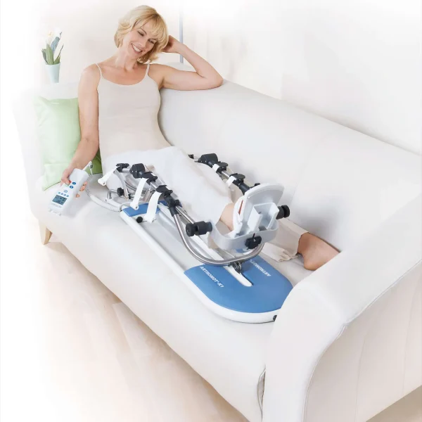 Kobieta korzystająca z szyny CPM do rehabilitacji kolana, siedząc wygodnie na kanapie.