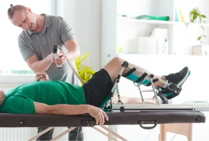 Pacjent podczas terapii z użyciem szyny CPM i elektroterapii, prowadzony przez specjalistę w gabinecie rehabilitacyjnym.