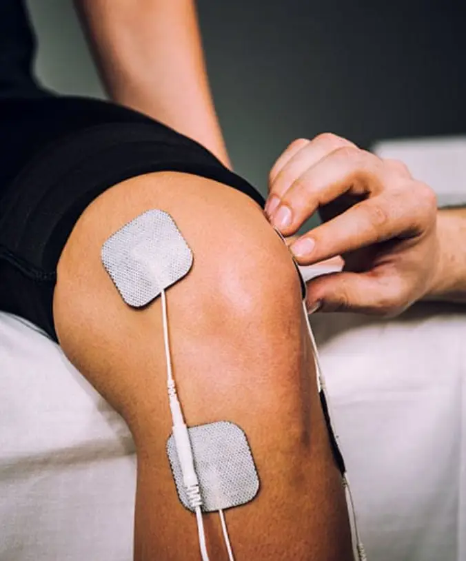 Zbliżenie na kolano poddawane elektroterapii z nałożonymi elektrodami adhezyjnymi.