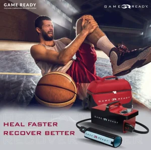 Koszykarz siedzący na boisku, trzymający się za kolano z bólem, z piłką obok niego. Na pierwszym planie widoczne jest urządzenie Game Ready z hasłem 'LECZYJ SZYBCIEJ, REGENERUJ LEPIEJ'.