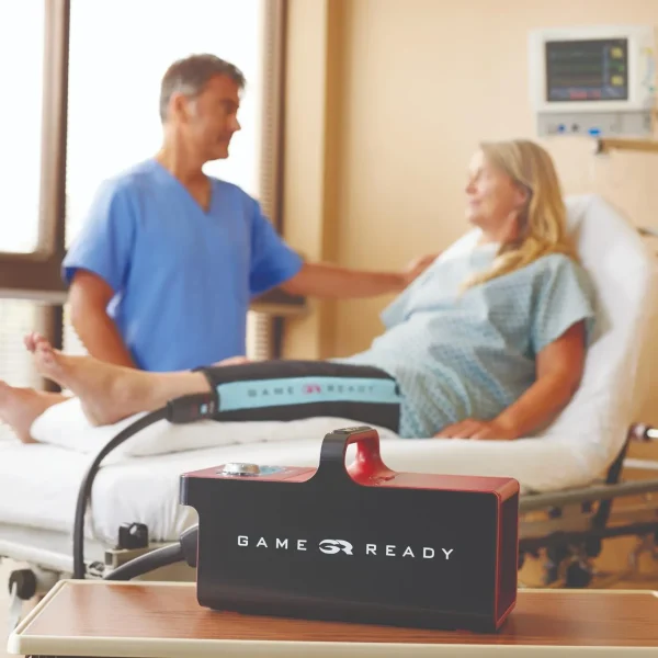 Pacjentka leżąca w szpitalnym łóżku z mankietem Game Ready na nodze, pod opieką lekarza.